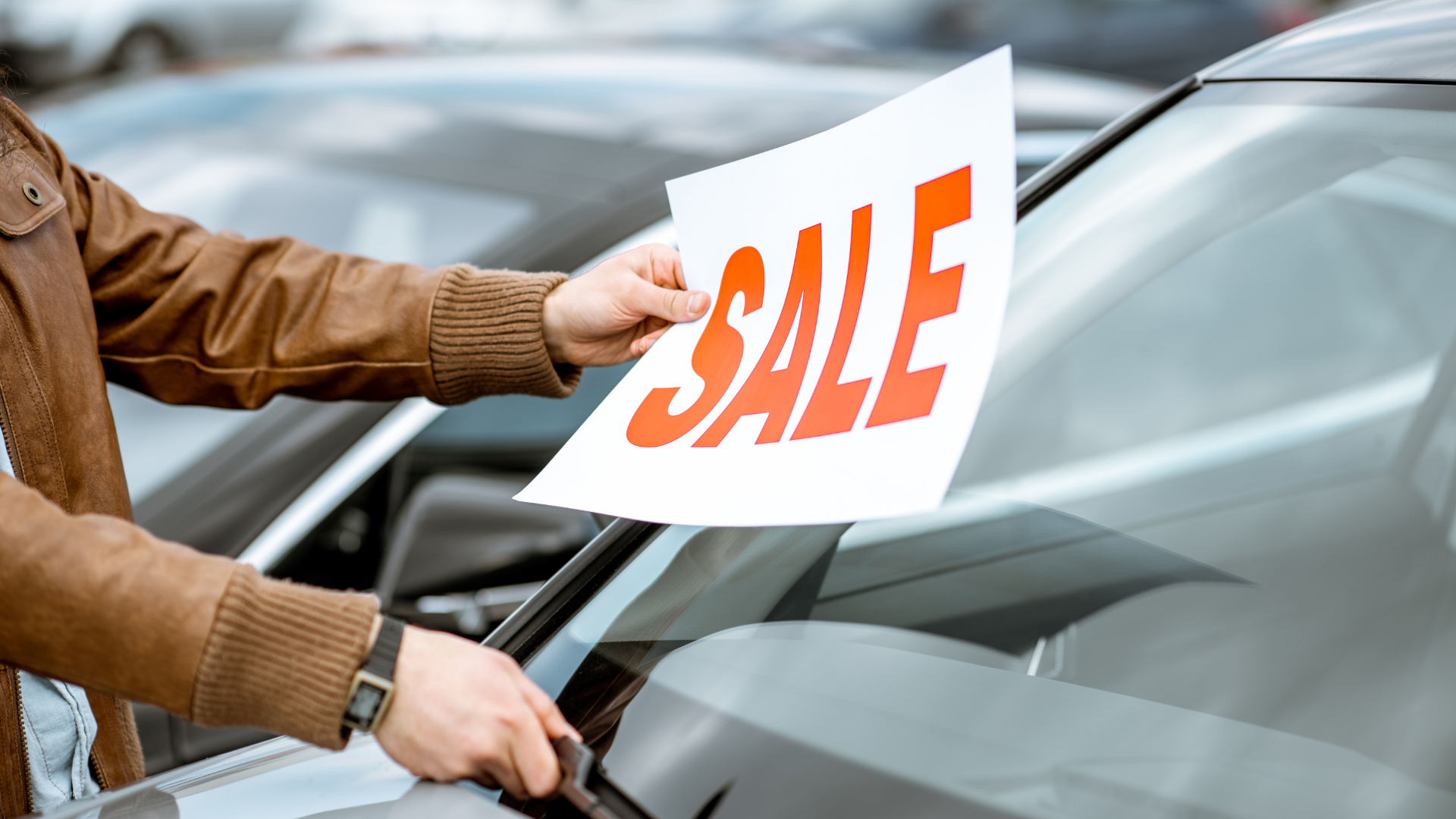 a car dealer putting and "sale" sign on the windshield of a car for an as-is sale