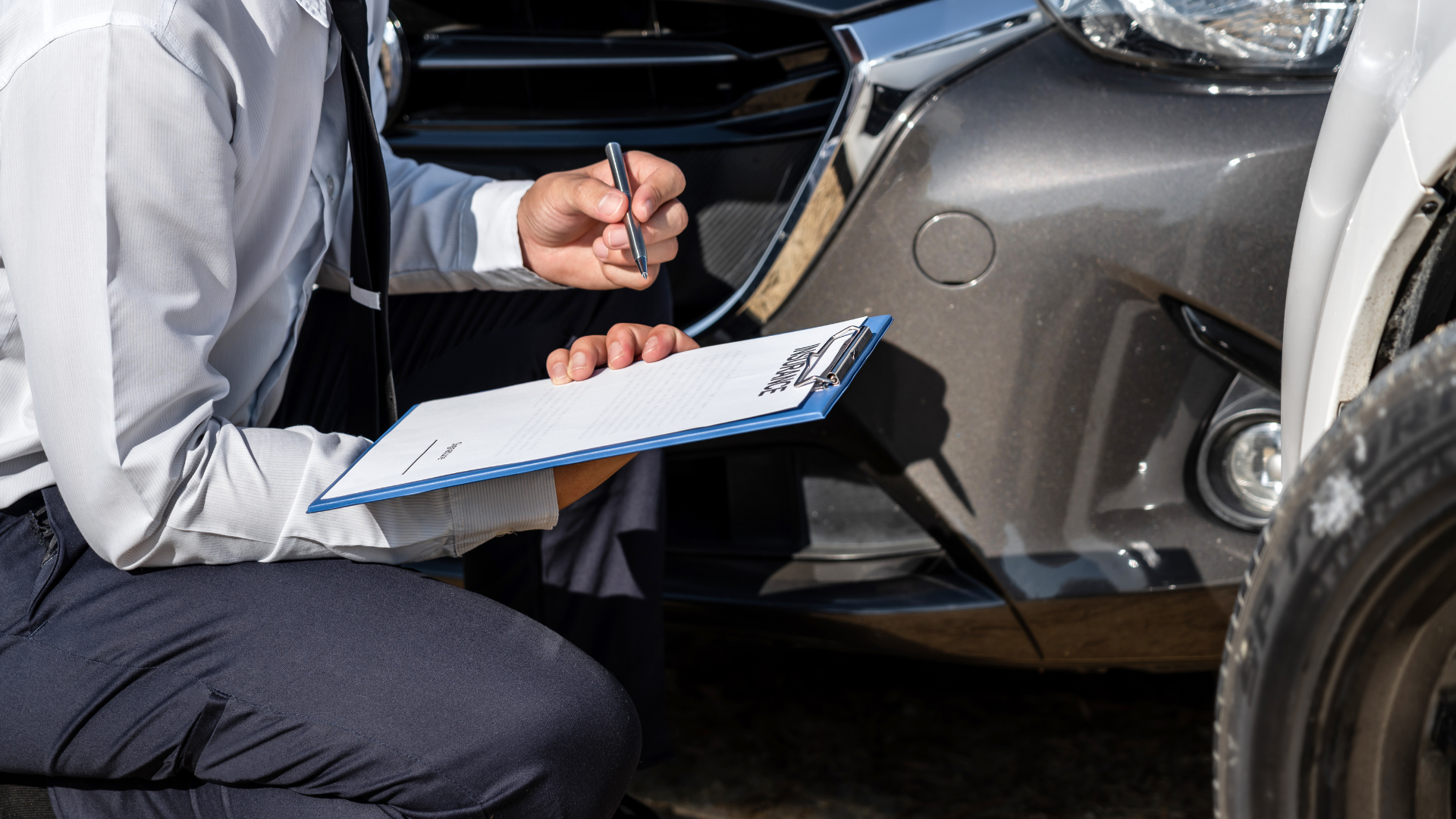 a gentleman crouched down filling out a vehicle history report for a car that is in an accident