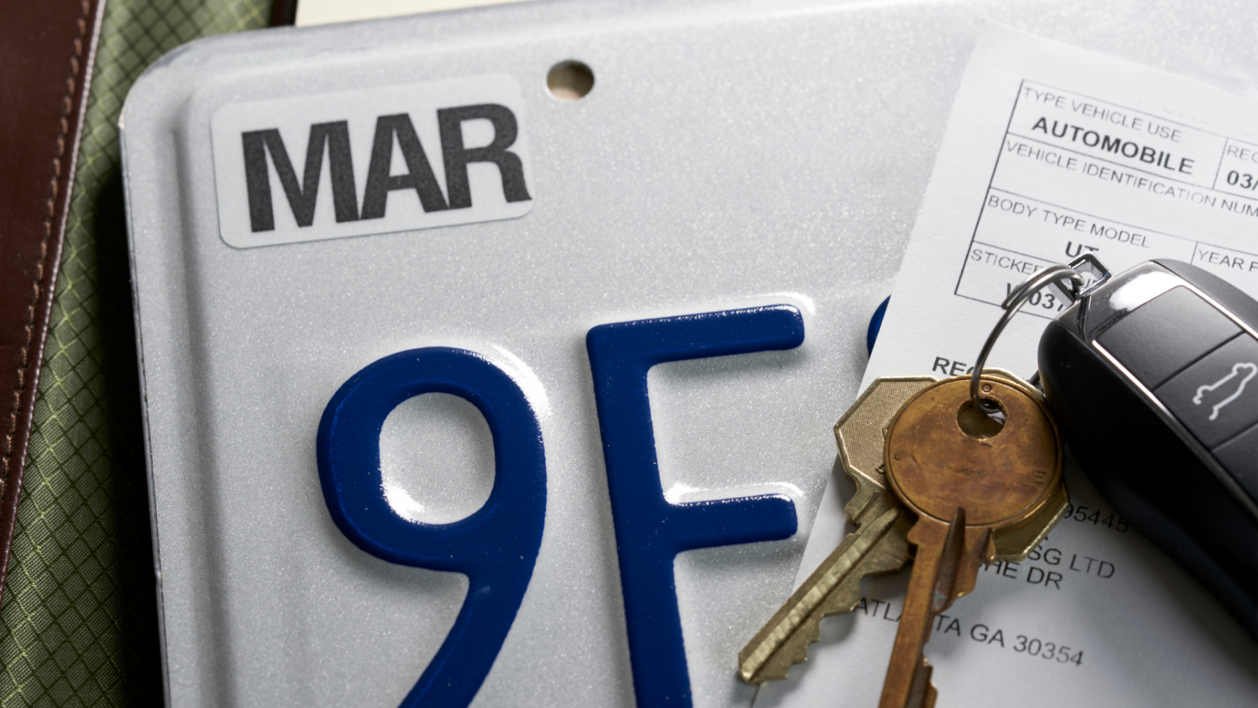 a close up of a license plate with a temporary tag paperwork covering half of it and a set of car keys on top.